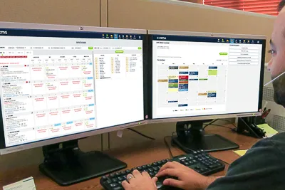 two hands typing on a keyboard with two computer monitors displaying CMS Enterprise moving software